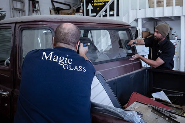 Technicians installing a back window in a vintage vehicle